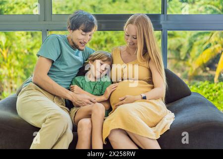 Gemütliche Familienzeit zu Hause, während schwangere Mutter, Vater und Sohn gemeinsame Momente auf dem Sofa genießen, herzzerreißende Erinnerungen schaffen und ihre Zeit schätzen Stockfoto