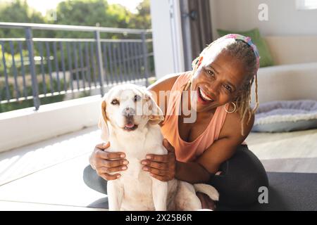 Afroamerikanerin umarmt ihren Hund zu Hause, beide sitzen auf der Matte, Kopierraum Stockfoto