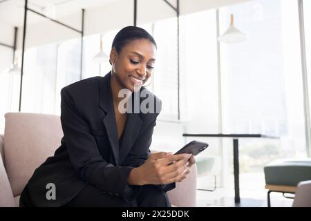 Positive schöne schwarze Geschäftsfrau mit Anwendung auf Handy Stockfoto