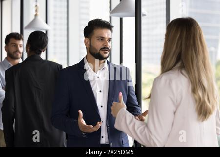 Ernsthafter junger indischer Geschäftsmann, der mit einer kaukasischen Kollegin spricht Stockfoto