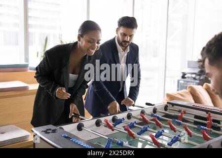Positiv aufgeregtes junges multiethnisches Paar von Profis, die Spielzeugfußball spielen Stockfoto