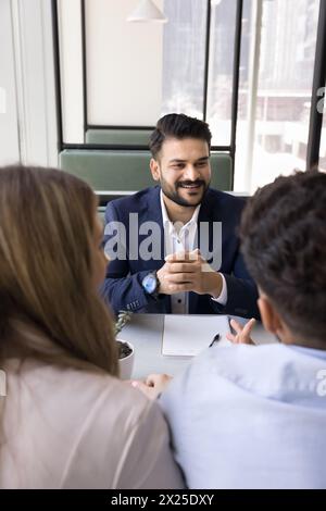Fröhlicher junger indischer Berater, der sich mit einem Paar trifft Stockfoto