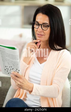 Reife Frau, die zu Hause ein Kreuzworträtsel macht Stockfoto