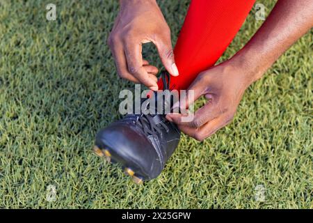 Afroamerikanischer junger männlicher Athlet, der Schnürsenkel auf einem Fußballfeld im Freien bindet, Kopierraum Stockfoto