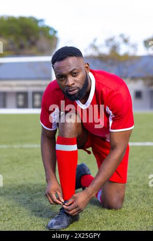 Afroamerikaner, junger männlicher Athlet, der seinen Schuh auf einem Fußballfeld im Freien bindet Stockfoto