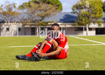 Afroamerikanischer junger männlicher Athlet, der draußen auf Gras sitzt, Schnürsenkel bindet, Kopierraum Stockfoto