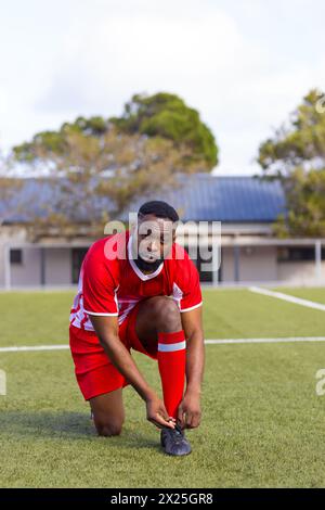 Afroamerikanischer junger männlicher Athlet, der Schnürsenkel auf dem Fußballfeld im Freien bindet, Kopierraum Stockfoto