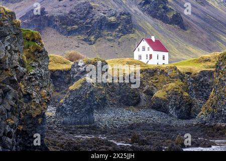 Arnarstapi, Island. Blick auf die zerklüftete Küste mit einem einsamen Haus. Herbstfarben mit Bergen im Hintergrund. Halbinsel Snaefellsnes. Stockfoto