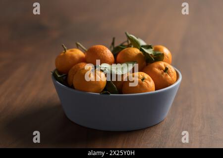 Kleine organische Mandarinen mit Blättern in Keramikschale auf Holztisch, flacher Fokus Stockfoto