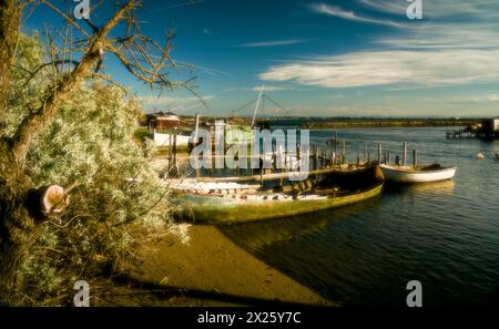 Das ruhige Wasser umschließt eine malerische Szene mit Fischerbooten und rustikalen Hütten entlang der Küste von Pialassa dei Piomboni, in der Nähe von Ravenna Stockfoto