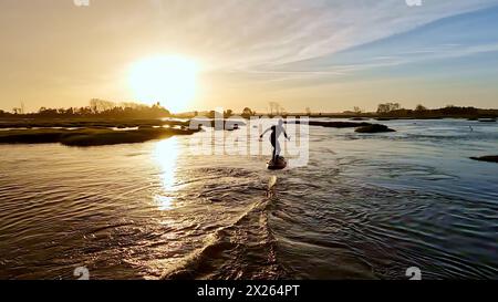 Tragflächenreiter gleitet mit seinem Brett in einem der Kanäle der Ria de Aveiro in Portugal während des Sonnenuntergangs über dem Wasser. Stockfoto