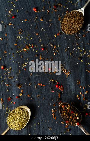 Alte Löffel mit verschiedenen Samen und Gewürzen auf schwarzem Hintergrund. Flach verlegt. Draufsicht. Speisekonzept. Dunkle Stimmungsfotografie. Stockfoto