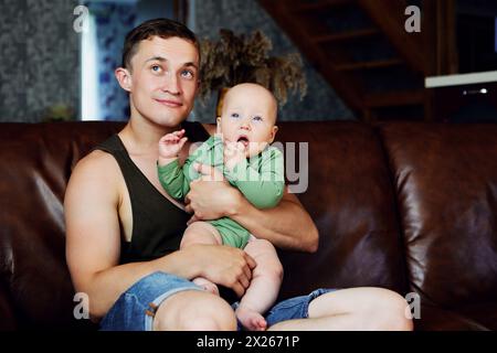 Vater mit Tochter in den Armen sitzt zu Hause auf Ledersofa. Stockfoto