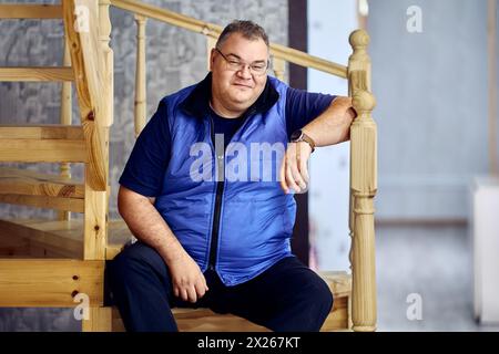 Ein übergewichtiger Weißer in seinen 40ern sitzt auf einer Holztreppe. Stockfoto