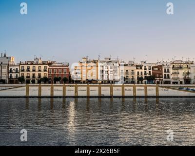 Farbenfrohe Gebäude, darunter Häuser und Geschäfte, blicken auf den Fluss Guadalquivir im Triana-Viertel der Analusischen Stadt Sevilla, Spanien, während der goldenen Zeit Stockfoto