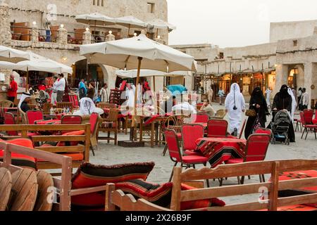 Doha, Katar. Eintritt zum kürzlich modernisierten „traditionellen“ Markt. Ein arabisches Café befindet sich auf der linken Seite. Eine verschleierte katarische Frau in einer Abaya schiebt Stockfoto