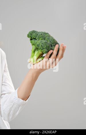 Konzept für gesunde Ernährung. Hand hält Brokkoli über grauem Hintergrund. Stockfoto
