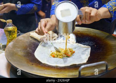 Tauchen Sie ein in die belebten Straßen Thailands mit dieser lebendigen Szene. Ein erfahrener Verkäufer bereitet auf fachmännische Weise knusprige Roti zu, ein beliebtes Street Food de Stockfoto