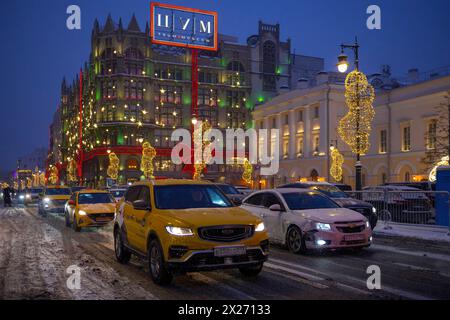 MOSKAU, RUSSLAND - 06. JANUAR 2024: Taxiwagen auf der Petrovka-Straße vor dem Hintergrund des zentralen Kaufhauses an einem verschneiten Januarabend Stockfoto