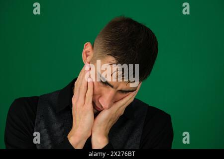 Müde Männer. Porträt von müden jungen Männern, die die Hände im Gesicht halten. Emotionen eines gutaussehenden Mannes auf grünem Hintergrund, Chromakey-Nahaufnahme, dunkles Haar, junger Mann Stockfoto