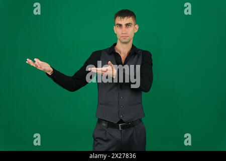 Emotionen eines gutaussehenden Mannes auf grünem Hintergrund, Chromakey-Nahaufnahme, dunkles Haar, junger Mann. Geschäftsmann, der auf etwas zeigt, als würde er etwas präsentieren Stockfoto