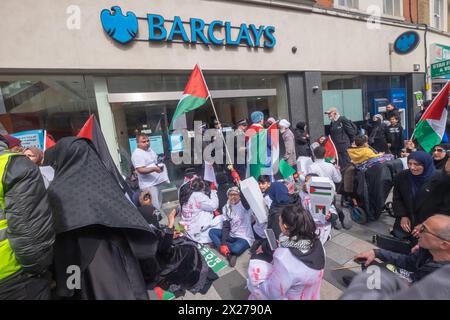 London, Großbritannien. 20. April 2024. Die Leute setzen sich vor Barclays und rufen die Polizei auf, um zwei Männer freizulassen, die sie festhalten. Eine Beerdigungsprozession in Ilford trägt kleine Särge, die um den Tod von über 34.000 Palästinensern, mehr als 13.000 Kindern, betrauern, wobei über 8.000 Vermisste wahrscheinlich unter Schutt in Gaza begraben sind. Es endete mit einer Kundgebung vor der Barclays Bank, die laut Aktivisten Israels Völkermord auf Palästinenser finanziert. Peter Marshall/Alamy Live News Stockfoto