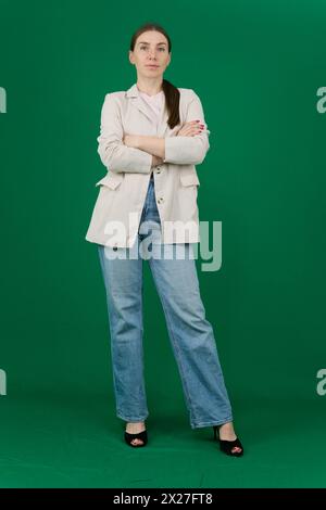 Schöne junge Frau auf grünem Hintergrund, Chromakey, Nahaufnahme einer Frau mit Emotionen in einer beigen Jacke, rote Maniküre, blaue Augen Stockfoto