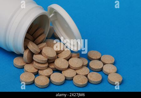 Medizin und Gesundheitskonzept. Gelb-braune Pillen Nahaufnahme. Aus einer weißen Plastikflasche verschüttete Pillen. Stockfoto
