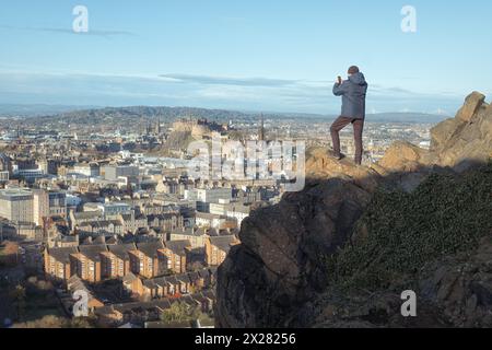 Ein Mann, ein Tourist, macht ein Handyfoto der Stadt Edinburgh vom Gipfel eines Berges. Arthurs Sitz. Edinburgh, Schottland, Vereinigtes Königreich Stockfoto