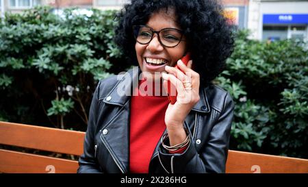Afroamerikanische Frau mittleren Alters mit lockigen Haaren, die in einer Stadt auf dem Handy spricht Stockfoto