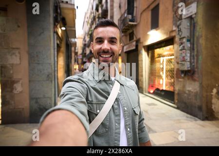 Junger Erwachsener glücklicher kaukasischer Mann, der ein lächelndes Selfie auf der touristischen Straße Madrids im Hintergrund macht. Stockfoto