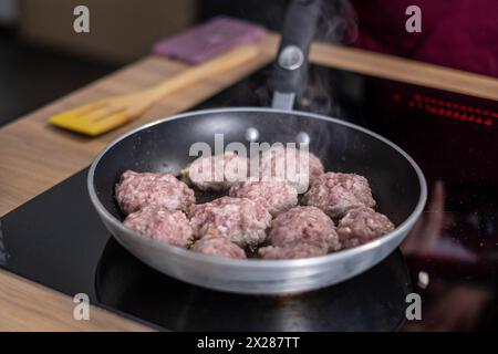 Dampf weht aus saftigen Fleischbällchen, die in einer modernen Antihaftpfanne gebräunt werden, eine Szene des aktiven Kochens, die für hausgemachte Mahlzeiten spricht. Hoch q Stockfoto