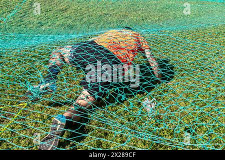 Ein Athlet, der bei einem Hindernisrennen unter einem Netz krabbelt Stockfoto