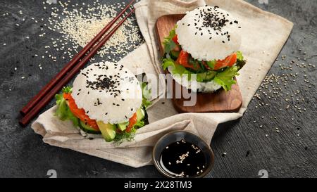 Asiatischer Sushi-Burger, Sojasauce, Essstäbchen auf dunklem Hintergrund. Trendiges Hybrid-Essen. Stockfoto