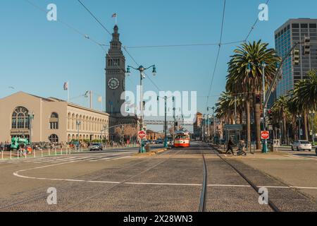 San Francisco, Kalifornien, 8. April 2024. Straßenbahnschienen führen zum Uhrenturm des Ferry Building, flankiert von Palmen auf dem Embarcadero. Stockfoto