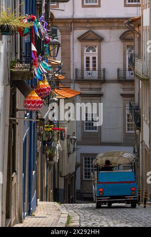 Blaues Tuktuk, das eine Kopfsteinpflasterstraße hinunter führt und Balkone alter Häuser in einem klassischen, alten Viertel von Porto bietet, dekoriert mit farbenfrohen Pappsteinen Stockfoto