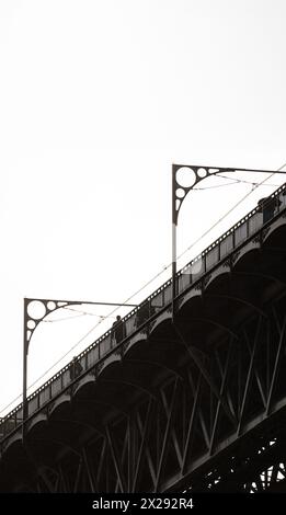 Silhouette von Menschen, die auf der oberen Plattform der Don Luis I Stahlbrücke in Porto laufen, mit Details der Metallkonstruktion und der durchgehenden Kabel Stockfoto