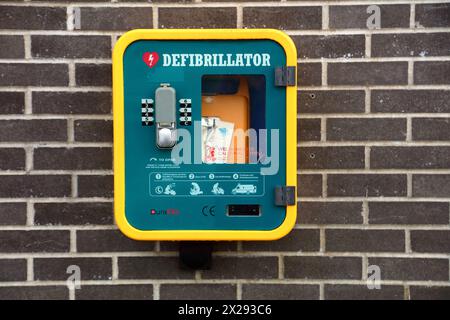 Ein Defibrillator an der Wand neben einigen großen Geschäften in der Stadt Tondu, wo viele Leute einkaufen und Fußfallen sind, ist schwer. Stockfoto