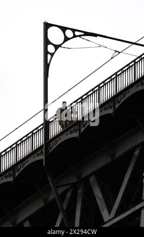 Ein paar Liebhaber, die auf der Spitze der Don Luis I Stahlbrücke in Porto spazieren, mit Details ihrer Metallstruktur mit Ornamenten unter einem wolkigen weiß Stockfoto