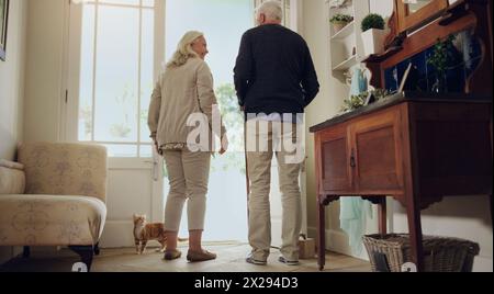 Lächeln, Seniorenpaar und Tür zu Hause zusammen zum Gespräch, zurück und gehen zum Spaziergang mit Haustier Katze. Rentner, älterer Mann und glückliche Frau in Stockfoto