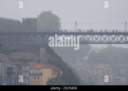 Menschen mit Regenschirmen und Regenmänteln gehen auf der oberen Plattform der Stahlbrücke Don Luis I mit der mittelalterlichen Mauer darunter, der Standseilbahn und dem o Stockfoto