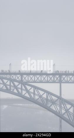 Menschen mit Regenschirmen und Regenmänteln gehen auf der oberen Plattform der Don Luis I Stahlbrücke und Autos fahren auf der unteren Plattform mit einer Person Stockfoto