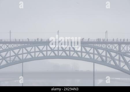 Menschen mit Sonnenschirmen, die auf dem oberen Bahnsteig der Don Luis I Stahlbrücke laufen, und Autos, die auf dem unteren Bahnsteig fahren, in Porto umgeben von Nebel Stockfoto