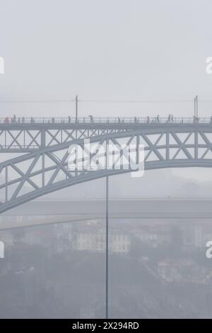 Menschen mit Regenschirmen und Regenmänteln gehen auf der oberen Plattform der Don Luis I Stahlbrücke und Autos fahren auf der unteren Plattform mit einer Person Stockfoto
