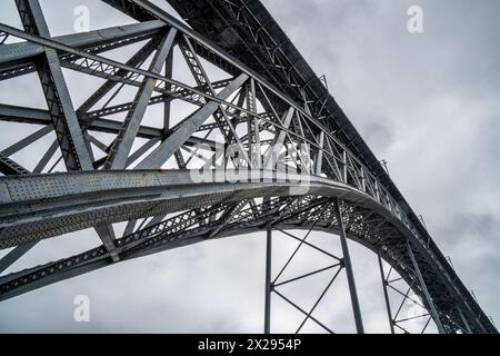 Perspektivische Ansicht mit Details von Nieten und Metallstruktur von unten auf der Don Luis I Stahlbrücke in Porto mit Regenwolken im Hintergrund. Stockfoto