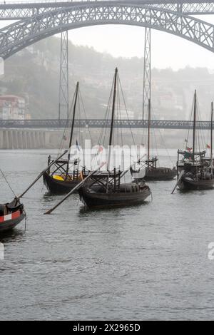 Im Douro-Fluss in Porto dockten Holzboote mit Weinfässern an, im Hintergrund die Stahlbrücke Don Luis I., die in Nebel gehüllt ist Stockfoto