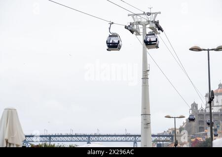 Zwei Seilbahngondeln hängen an hängenden Stahlseilen mit dem Mechanismus, der Touristen mit der Don Luis I Brücke im Hintergrund transportiert, darunter Stockfoto