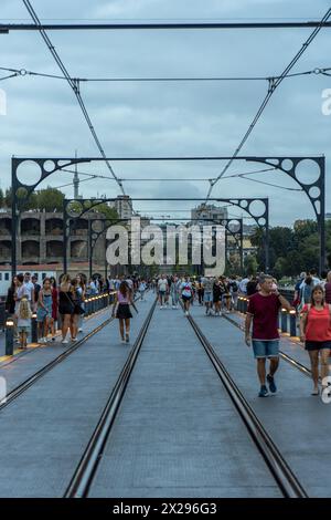 Dom Luis Brücke in der Abenddämmerung, unter einem bewölkten Himmel mit vielen Touristen, die an den Seiten spazieren, lachen und eine gute Zeit mit der Metro von Porto haben Stockfoto