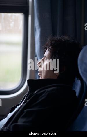 Eine besinnliche ältere Frau schaut aus dem Fenster eines fahrenden Zuges Stockfoto