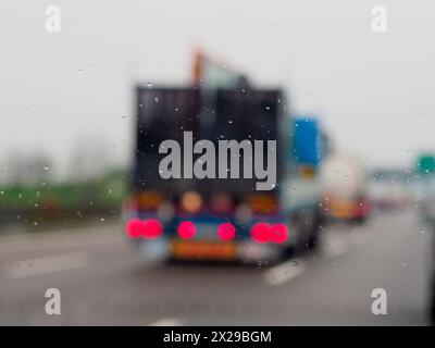 Ein verschwommenes Bild einer belebten Straße mit Autos und einem LKW. Der Regen macht die Windschutzscheibe der Autos und des Lkws nass Stockfoto